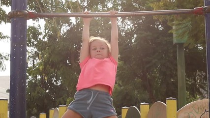 Little girl pulls up on horizontal bar in summer city park. - Powered by Adobe