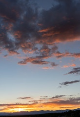 Obraz premium Orange Tinted Dark Clouds with Pale Blue Sky and Distant Mountains at Sunset