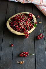 red currant in wooden plate on dark wooden background.