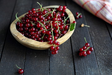 red currant in wooden plate on dark wooden background.