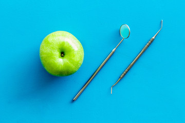 stomatologist mirror and apple on blue doctor's office desk background top view