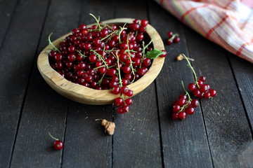 red currant in wooden plate on dark wooden background.