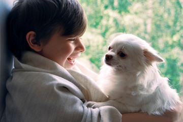 happy boy sitting on a windowsill with a dog in his arms