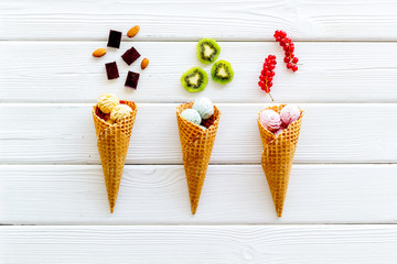 Gelato in waffle cone with kiwi, hazelnut, chocolate and wineberry on white wooden backgroung top view