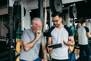 Senior man exercising in gym with his personal trainer.