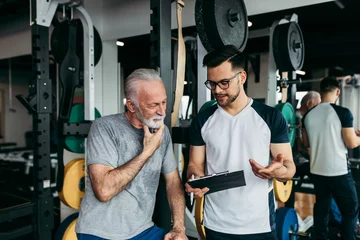 Türaufkleber Senior man exercising in gym with his personal trainer. © hedgehog94