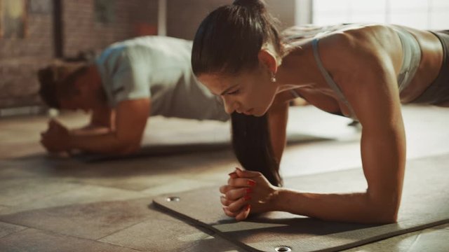 Strong Masculine Male and Two Fit Atletic Women Hold a Plank Position in Order to Exercise Their Core Strength. Man is Exhausted and is Struggling with Training. They Workout in a Loft Gym.