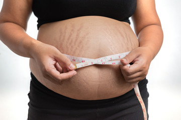 Closeup of Asian pregnant woman Is using a belly scale isolated on white background