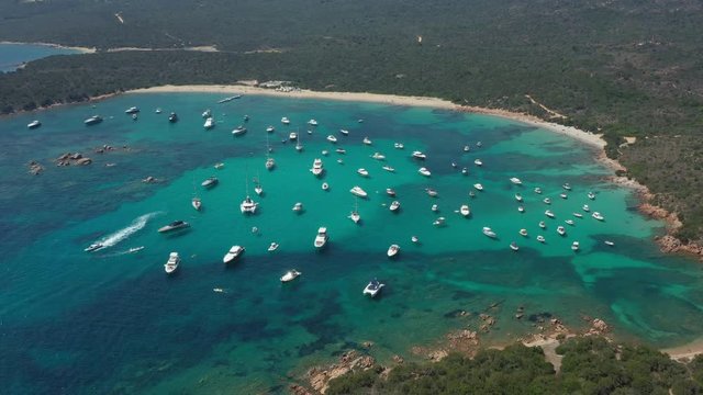 View from above, stunning aerial view of the beautiful Cala Di Volpe bay full of boats and luxury yachts. A turquoise sea bathes the green and rocky coasts. Emerald Coast, Sardinia, Italy.
