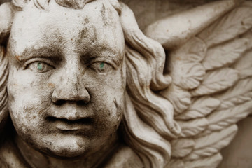 Fragment of ancient statue of angel with wings and green eyes