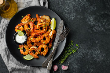 Grilled shrimps or prawns served with lime, garlic and white sauce on a dark concrete background. Seafood. Top view with copy space. Flat lay