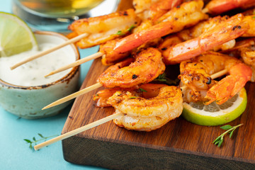 Grilled shrimp skewers or langoustines served with lime, garlic and sauce on a light blue concrete background. Seafood