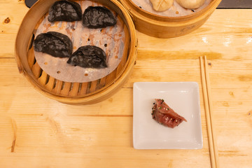 White, black and red pork meat, shrimps and mushroom steamed dumplings on a wooden table in a wooden steamer in an asian restaurant or chinese bar with dumplings. Two bottles on the nackground of soy