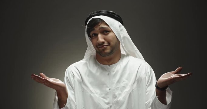 Arabian man looking at camera and positively smiling, throwing his hands wide in surprise or misunderstanding, isolated on black background close up 4k