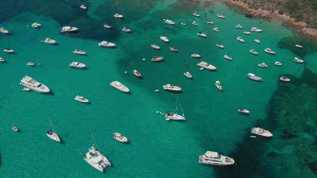 View from above, stunning aerial view of the beautiful Cala Di Volpe bay full of boats and luxury yachts. A turquoise sea bathes the green and rocky coasts. Emerald Coast, Sardinia, Italy.