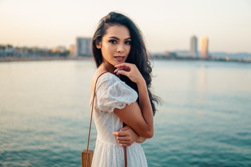Beautiful girl in the white dress waiting along the sea promenade. Elegance and tenderness concept
