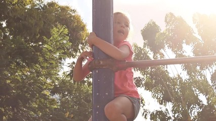 Little girl pulls up on horizontal bar in summer city park - Powered by Adobe