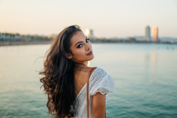 Beautiful girl in the white dress posing and waiting along the sea promenade. Elegance and tenderness concept