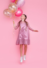 Happy teenage girl jumping high with balloons isolated on pink background