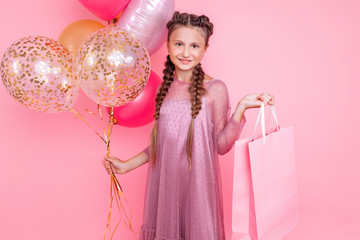 Happy girl with balloons and shopping bags posing on a pink background