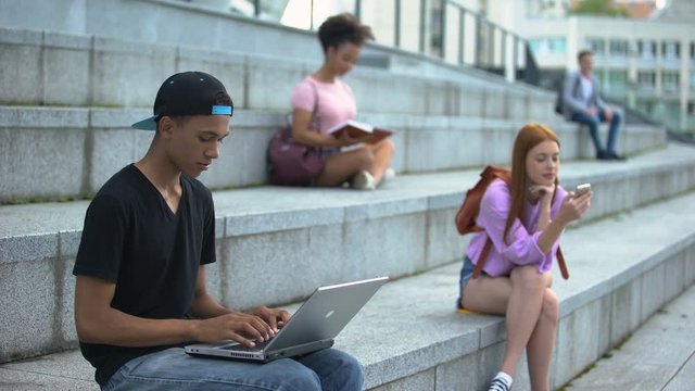 Young student typing laptop sitting campus stairs, digital generation, freelance