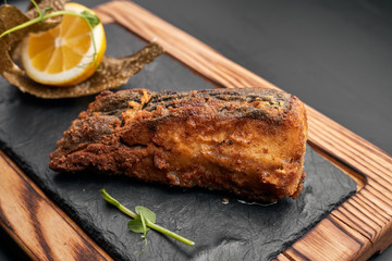 Fried fish on black slate on a wooden board on a dark background. Flounder
