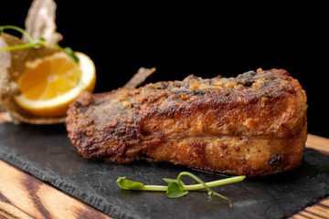 Fried fish on black slate on a wooden board on a dark background. Flounder