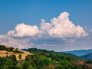 Rain clouds - Cumulonimbus - forming in the blue sky over hilly landscape
