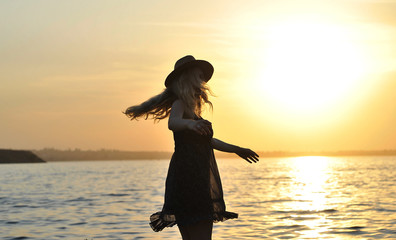 Fototapeta premium Stylish woman in hat walks on the beach at sunset.