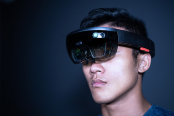 The Asian young man with virtual reality glasses. Experience VR hololens headset in studio with...