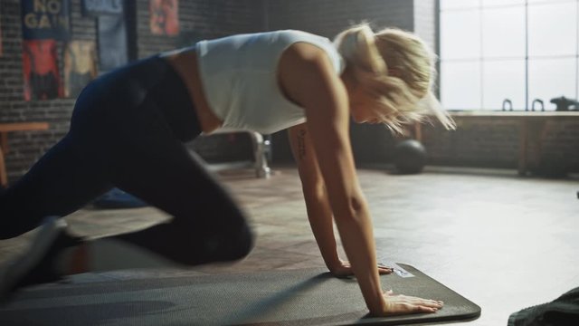 
Beautiful and Young Girl Uses Smartphone App to Setup Timer For Her Exercise and Starts doing Running Plank on Her Fitness Mat. Athletic Woman Does Mountain Climber Workout in Stylish Hardcore Gym