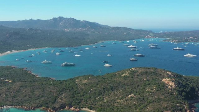 View from above, stunning aerial view of the beautiful Cala Di Volpe bay full of boats and luxury yachts. A turquoise sea bathes the green and rocky coasts. Emerald Coast, Sardinia, Italy.