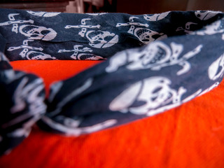 Scarf with skull and crossbones like a headband lying on orange cloth - selective focus