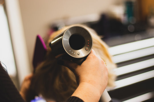 Young professional hair stylist brushing and blow-drying a blonde woman's hair in a salon