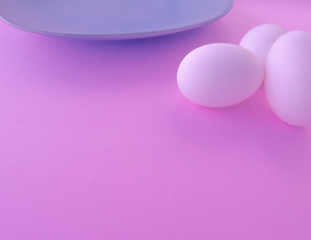 A light blue neutral plate with white chicken eggs on a neutral pink background. Free space to write.