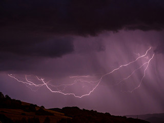 Naklejka na ściany i meble Storm with lightning over hilly landscape - Long exposure at night