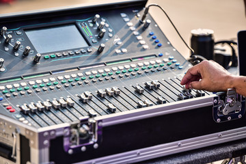 The DJ is adjusting the volume of the sound. Professional audio mixing console