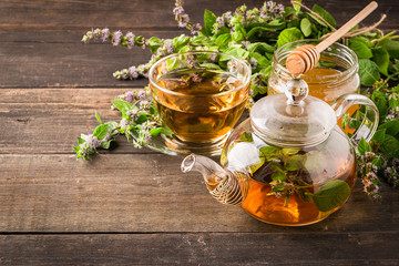 Tea with fresh leaves of lemon balm mint in a cup and teapot on a wooden rustic background. Healing...
