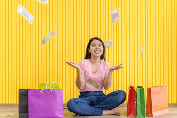 Asian young women wear pink t-shirts and jeans, sitting on the floor with paper bags and banknotes falling down.