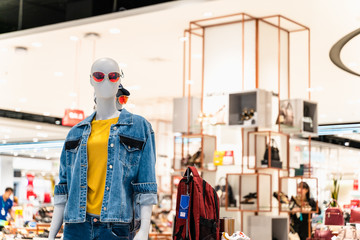 Female puppets wearing sunglasses, shirts and jeans with luggage and sneakers in department store.