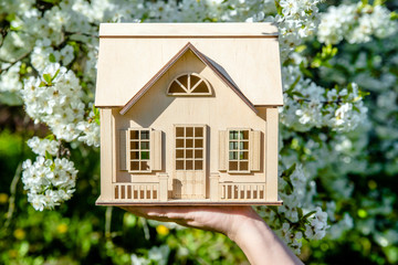 The girl holds the house symbol against the background of blossoming cherry 