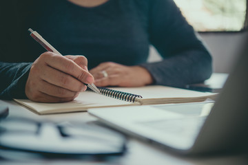 The hand of a man holding a pen and taking notes in a notebook.