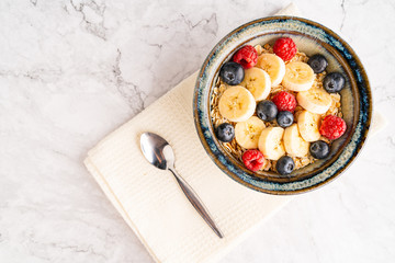 Fresh milk oatmeal with sliced blueberries and raspberries in a bowl on the white marble floor.
