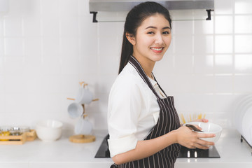 Portrait of beautiful asian woman or housewife is cooking food for family in white kitchen