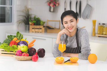 Portrait of beautiful asian woman, housewife with orange juice in white kitchen with plenty of...