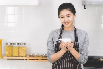 Portrait of beautiful Asian woman wearing an apron smiling and holding a cup of hot coffee