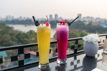 Passion fresh fruit juice with ice on outdoor table in cafe and bar. Pineapple and red dragon fruit. Urban lake on background