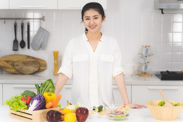 Portrait of beautiful asian woman is sitting in the bright white kitchen. wife or housewife is preparing to cook healthy food which consists of a variety of fruits and vegetables for the family.