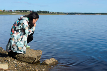 Modern sad girl Yakut looks at the water of the river vilyu contaminated with waste from diamond production in the North of Russia in Yakutia in the village of Suntar.
