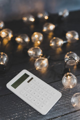 calculator on wooden desk surrounded by lightbulb string lights, good ideas for finance